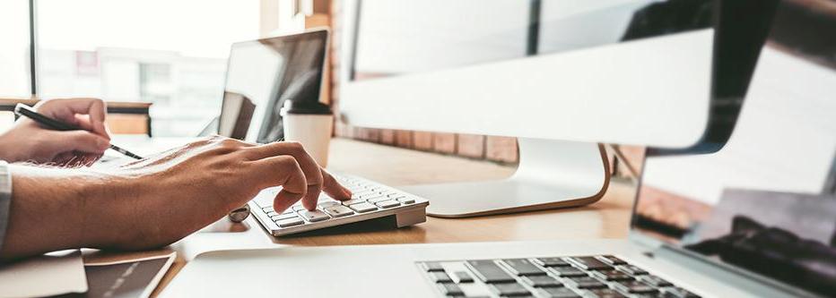 Man typing at a desktop Mac computer with a laptop and IPad nearby